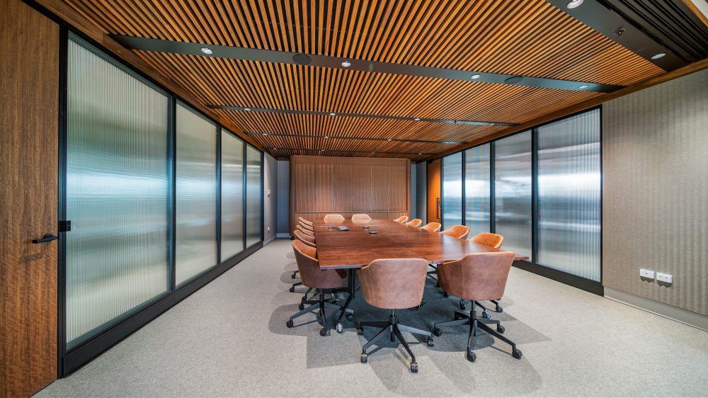 Boardroom enclosed by bespoke aluminium framed partitions in feature reeded glass, beneath a timber slat ceiling