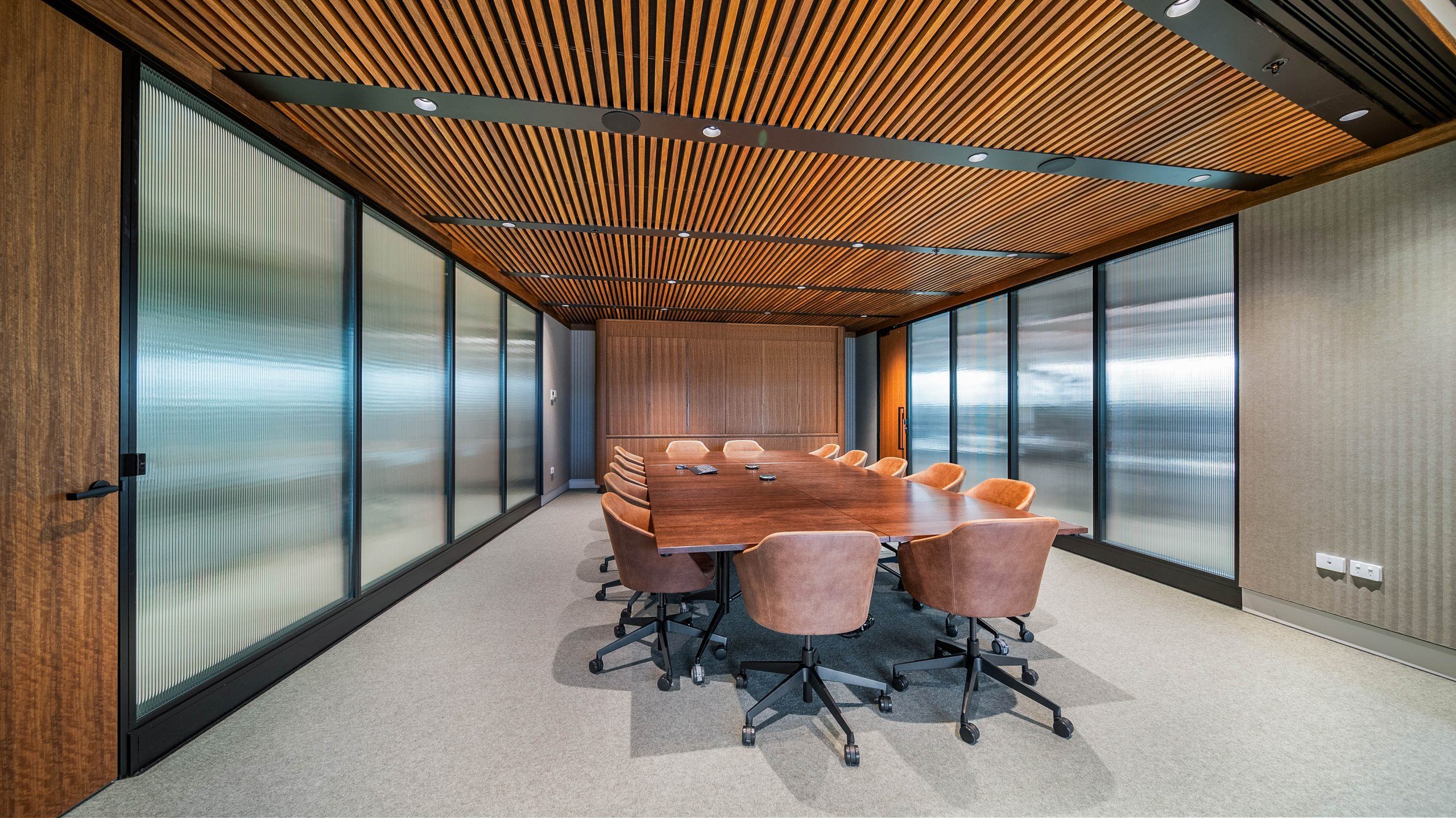 Boardroom enclosed by bespoke aluminium framed partitions in feature reeded glass, beneath a timber slat ceiling