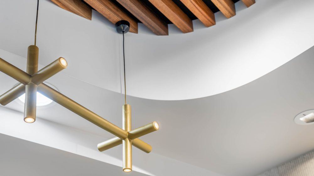 Curved plasterboard bulkhead meeting the timber slat ceiling, with brass pendant lighting