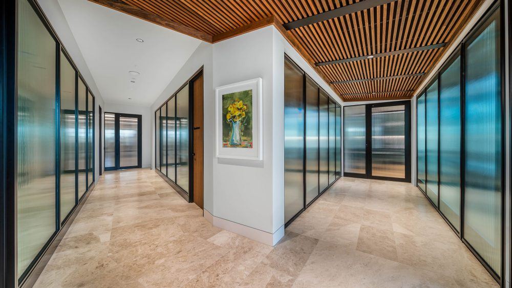 Faceted run of aluminium framed glazed office fronts lining a corridor with a timber slat ceiling