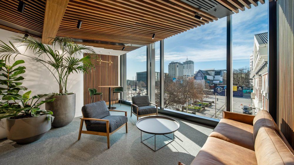 Lounge seating and planting beside full-height glazing under a timber slat ceiling