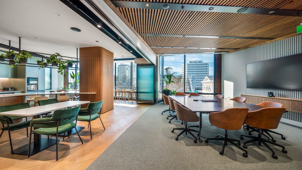 Meeting table and adjoining breakout beneath a timber slat ceiling, framed by glazed partitions